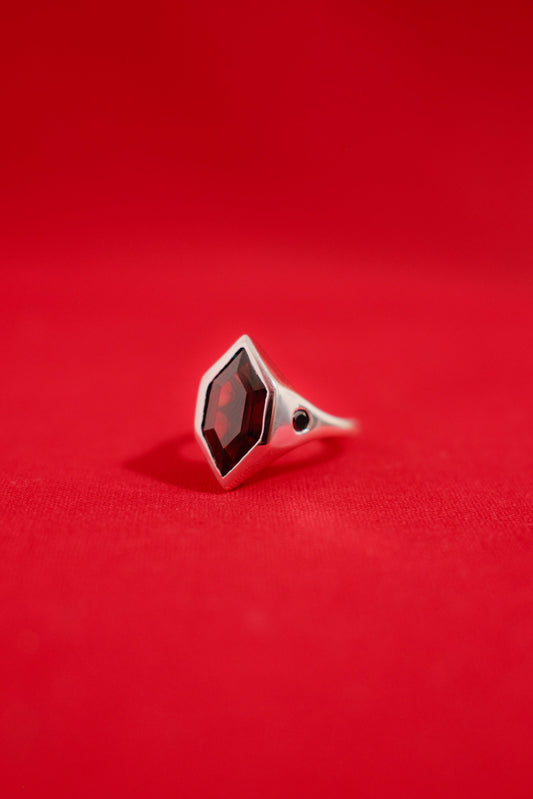 Solid white gold ring with a garnet gemstone on a red background
