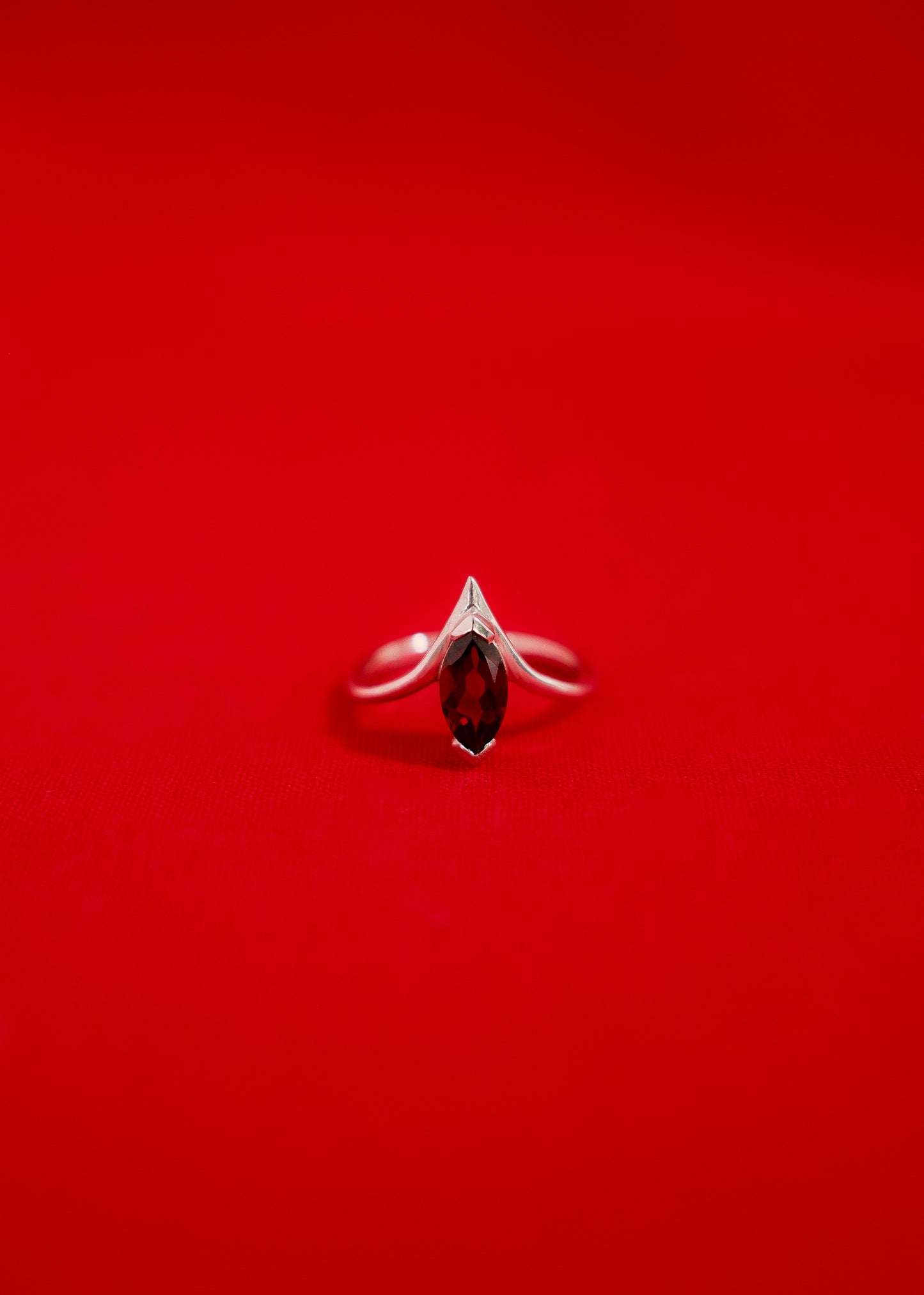 White gold ring with a garnet gemstone on a red background