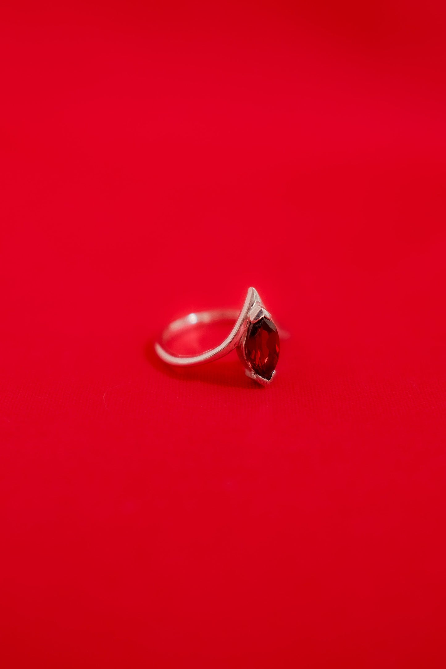 White gold ring with a garnet gemstone on a red background