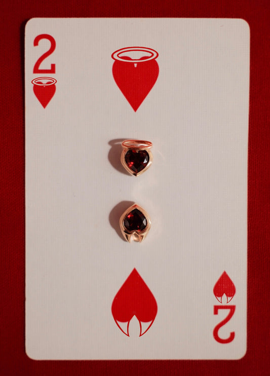 Yellow gold earrings with heart cut garnet gemstones set in an angel and devil style setting on a playing card with red hearts and number 2.
