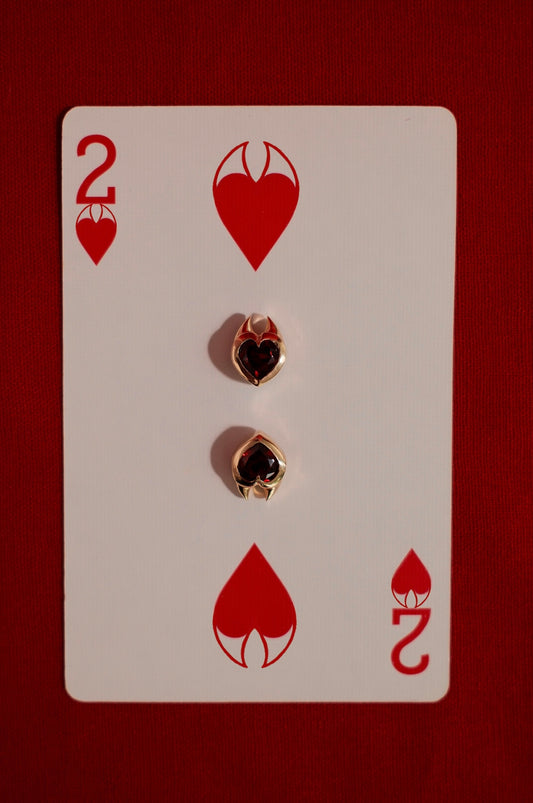 Yellow gold earrings with heart cut garnet gemstones in devil style setting on a playing card with the number 2 and heart symbols.